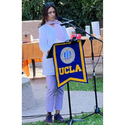 Anjali Prabhu stands in front of an outdoor podium decked with a UCLA banner.