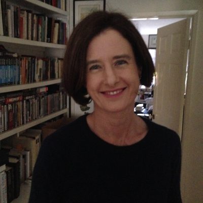 Romy Sutherland stands in a hallway lined with bookshelves.
