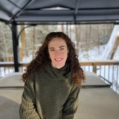 Ana Ugarte wears a green sweater and stands inside an outdoor patio with snow in the background.
