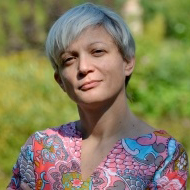 Zrinka Stahuljak wears a colorful shirt in front of green foliage.