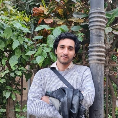 Diaa Alsersawi, wearing a grey sweater, leans on a wood post.