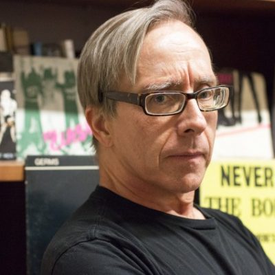 Kenneth Reinhard, swearing a black shirt, seated in front of a bookshelf.