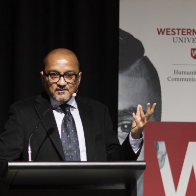 Aamir Mufti stands before a podium at a conference.