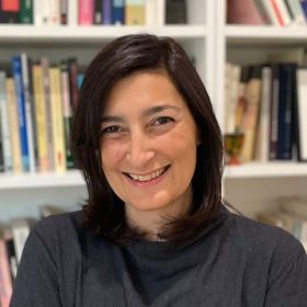 Yasemin Yildiz, wearing a grey top, stands in front of a bookshelf.